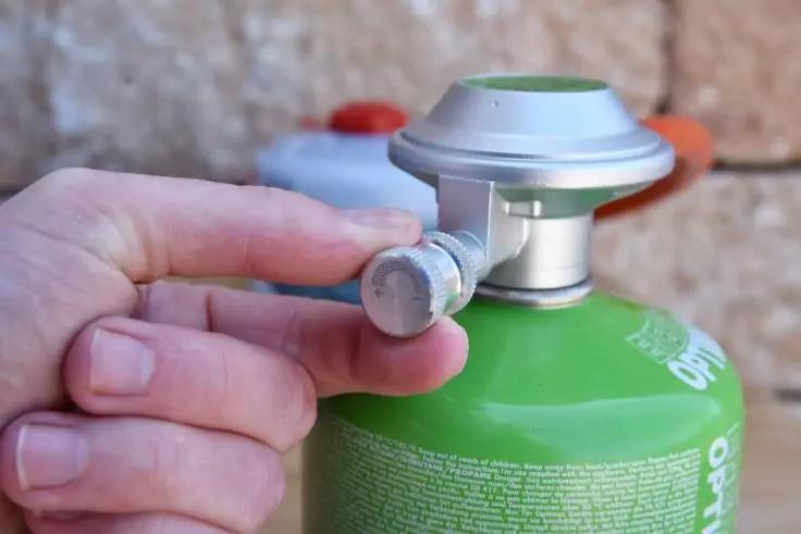 Mano tocca una valvola argentata su una bomboletta verde; sfondo sfocato