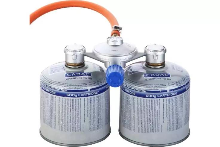 Due cartucce di gas argentate con etichette blu, collegate da un collettore argentato e un tubo arancione