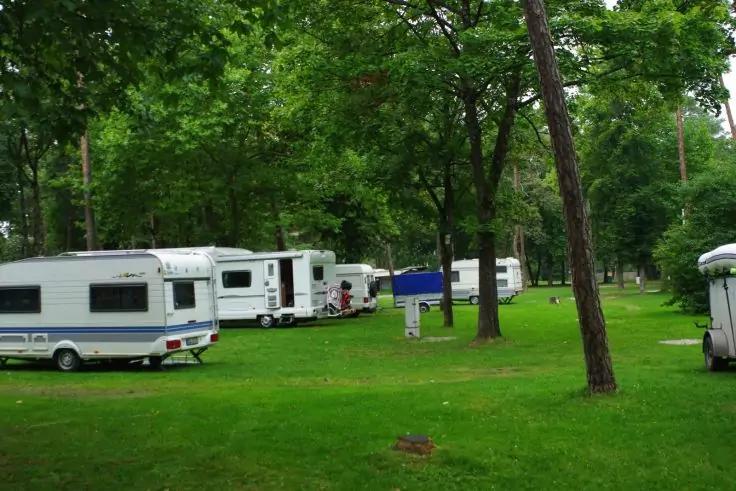 Pi&ugrave; caravan bianchi su un prato verde tra alberi alti, un piccolo tendalino blu visibile sullo sfondo