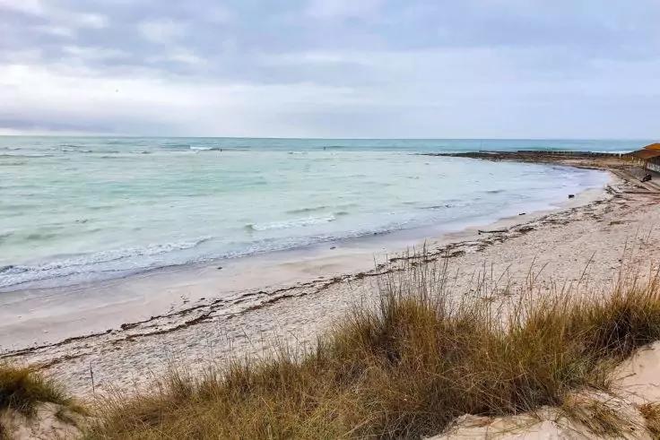 Spiaggia di sabbia con dune e erba secca, mare calmo e cielo nuvoloso