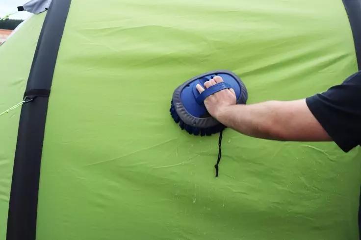 Braccio con maglietta nera a maniche corte che tiene un oggetto rotondo blu con maniglia contro una superficie curva verde con due strisce nere