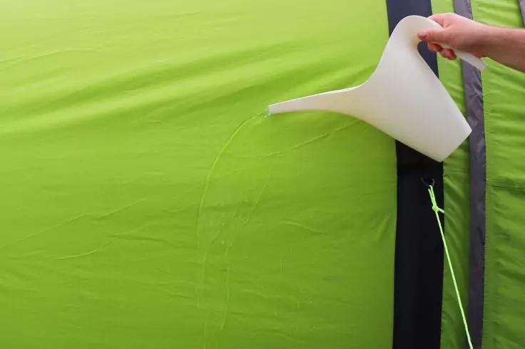 Mano che tiene un annaffiatoio bianco che versa acqua su un tessuto verde brillante con una striscia nera verticale