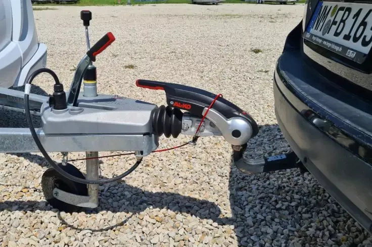 Gancio di traino del rimorchio sulla palla di traino di un'auto, paraurti e superficie ghiaiosa visibili