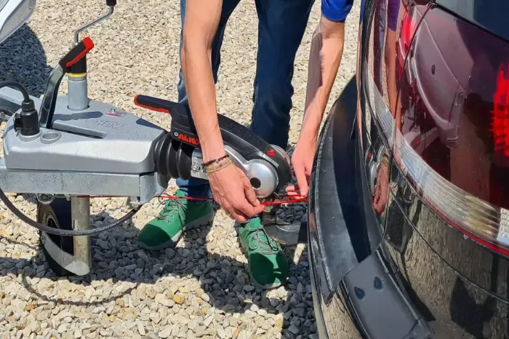 Braccia e gambe di una persona che fissa un gancio di rimorchio al retro di un'auto scura su ghiaia