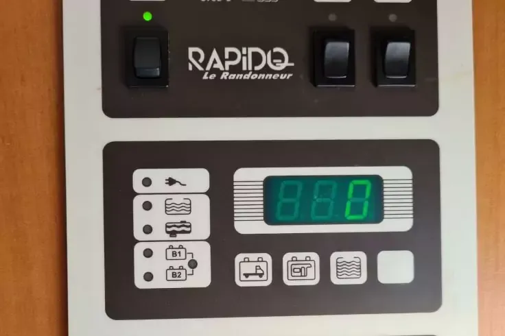Pannello grigio-bianco con tre interruttori neri a bilanciere in alto, spia verde, scritta "RAPIDO le Randonneur", sotto un display rettangolare con cifre verdi "888" e diversi piccoli simboli quadrati e pittogrammi