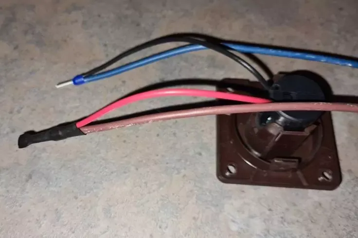 Piastra di plastica quadrata marrone con un elemento rotondo e pi&ugrave; fili isolati rossi, blu e neri; l'estremit&agrave; di un filo blu &egrave; spelata