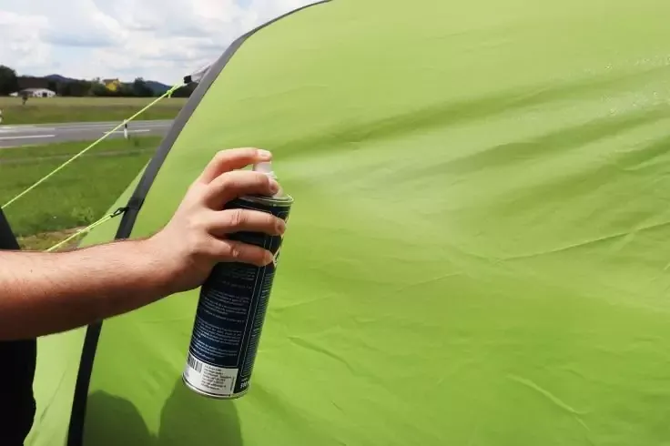 Avambraccio e mano che tengono una bomboletta spray accanto alla parete di una tenda verde