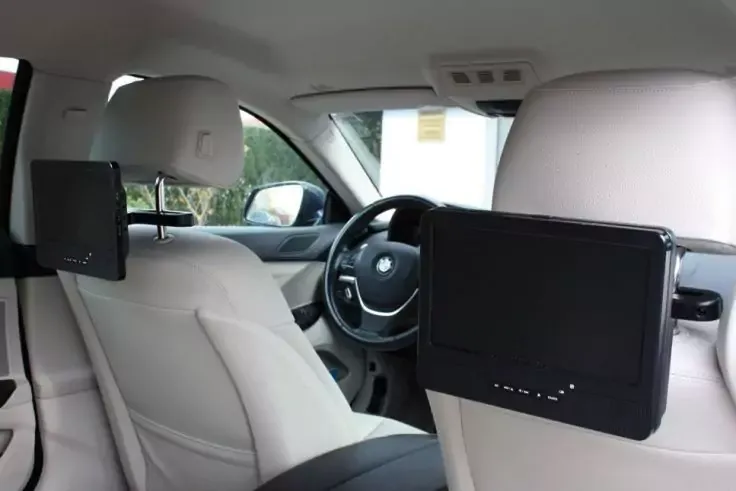 Interno di un'auto con sedili in pelle chiara, volante, cruscotto e due schermi montati sul retro dei sedili anteriori