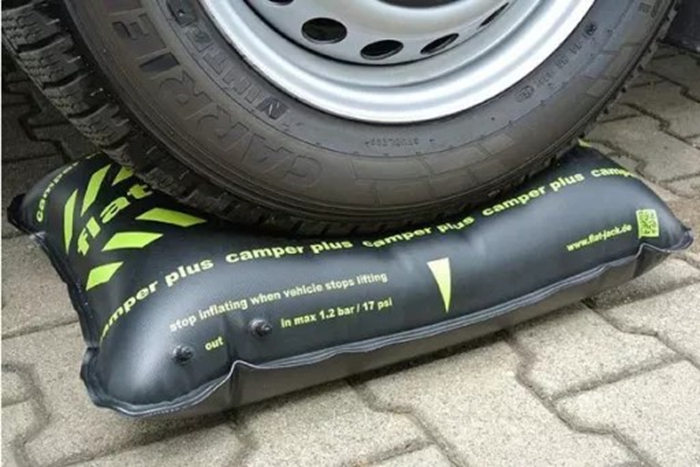 Voertuigband op een zwart opblaasbaar hefkussen met groene markeringen en witte tekst op een geplaveide ondergrond