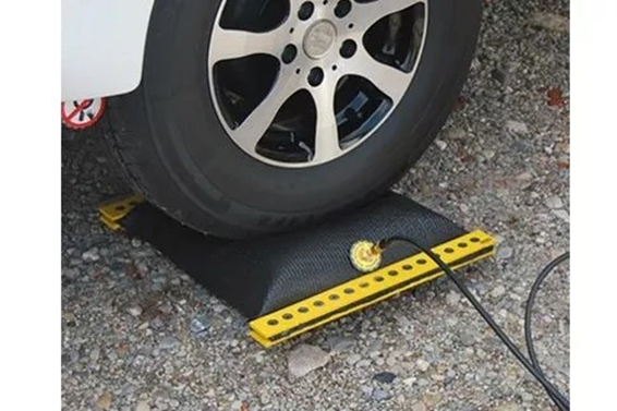 Autoband op een zwart rechthoekig rubberen pad met een gele rand en een zwarte kabel op grind