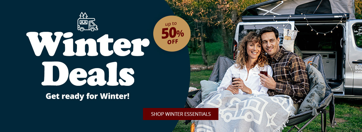 Two people sit in the open rear of a camper van, under a blanket with white camper silhouettes; left side dark background with large text 'Winter Deals', smaller text 'Mach dich bereit für den Winter', round badge 'bis zu 52% sparen' and red button 'Zu den Angeboten'. Grass and trees in the background