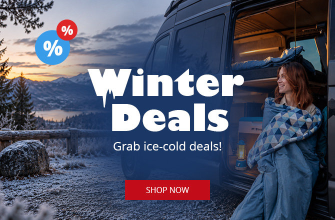 Snow‑covered mountain landscape with a lake, parked camper van with open door, a person wrapped in a blanket sitting in the doorway, interior lit, overlaid text 'Winter Deals', percent icons and a red button reading 'Zu den Angeboten'