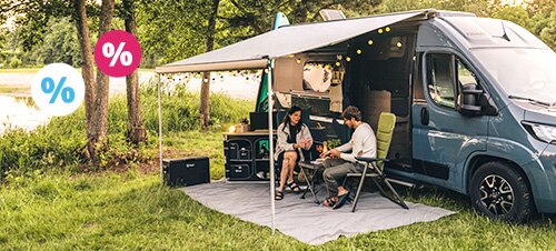 Paar sitzt in einer Hängematte am See neben einem Camper