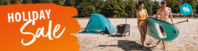 Two people carrying a stand-up paddleboard on a sandy beach; in the background a blue tent, cooler and trees; left an orange banner with the text Urlaubs Sale; top right a blue percent symbol