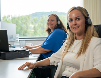 Drei Personen mit Headsets arbeiten an Computern in einem Büro