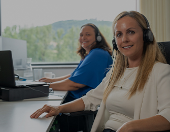 Drei Personen mit Headsets arbeiten an Computern in einem Büro
