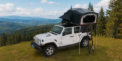 Aufgeklapptes Berger Klapp-Dachzelt auf einem Jeep in den Bergen auf einer Lichtung mit Tannen.