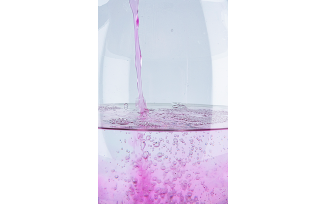 Liquido rosa versato in acqua chiara, bolle che salgono