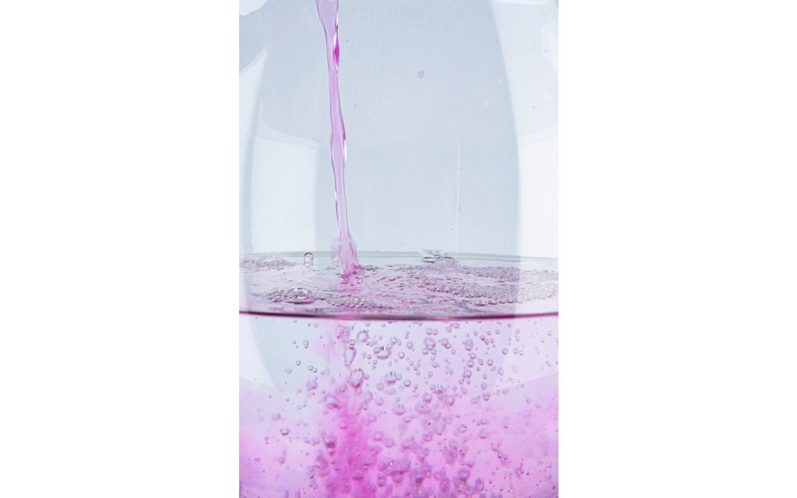 Liquido rosa versato in acqua chiara, bolle che salgono