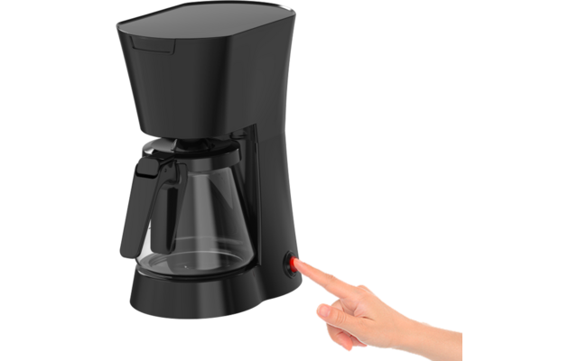 Cafetera de goteo negra con jarra de vidrio; una mano derecha pulsa un botón de encendido rojo