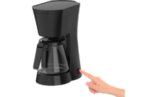 Cafetera de goteo negra con jarra de vidrio; una mano derecha pulsa un botón de encendido rojo
