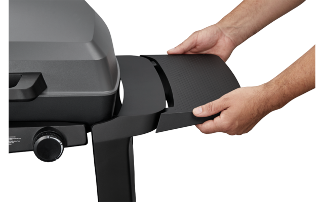 Two hands hold a black side panel next to a gray gas grill on a white background
