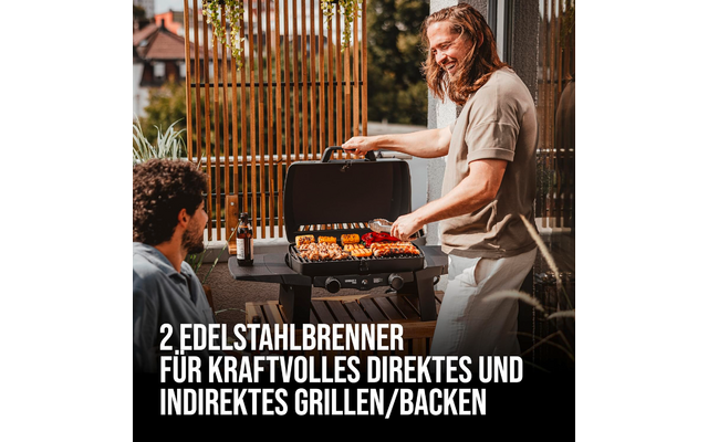 Two men on a balcony; one stands at a grill turning skewers of vegetables and meat, the other sits nearby with a beer bottle