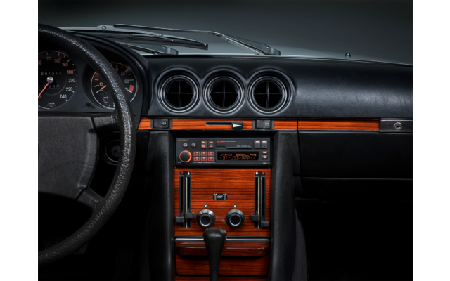 Armaturenbrett eines Autos mit drei runden Lüftungsöffnungen, Holzfurnier, Mittelkonsole mit Radio, Bedienelementen, Schalthebel und links sitzendem Lenkrad