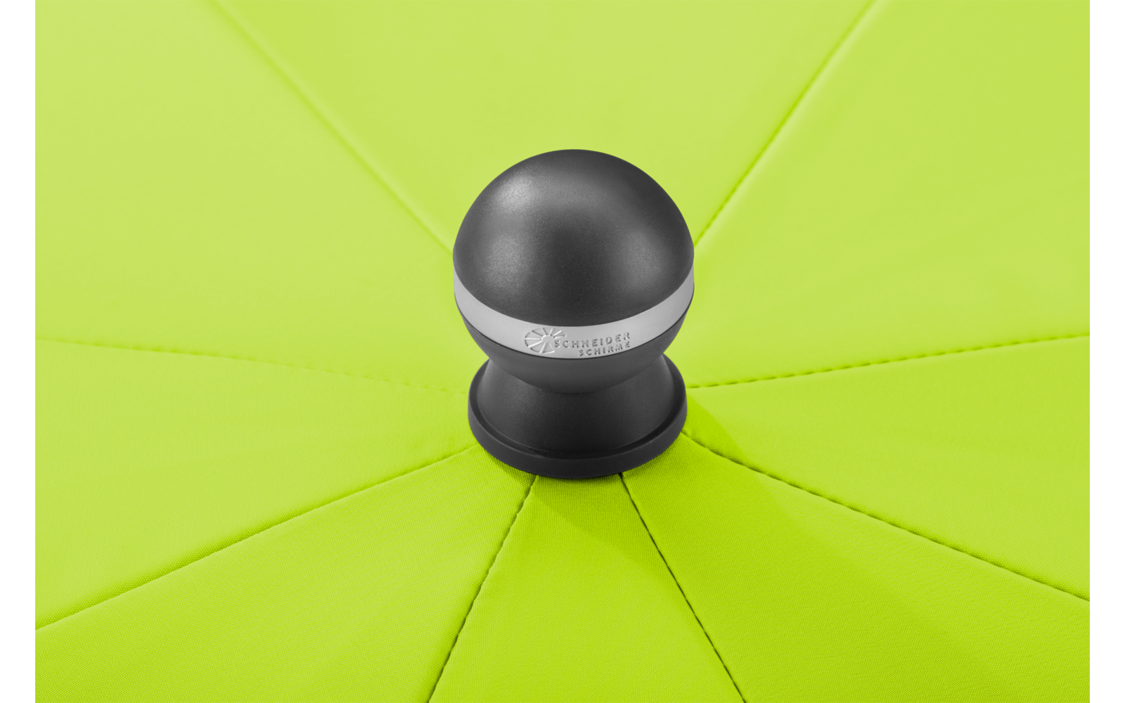 Nahaufnahme eines hellgrünen Schirmdachs mit radialen Nähten und einem schwarzen runden Knauf mit silbernem Ring in der Mitte