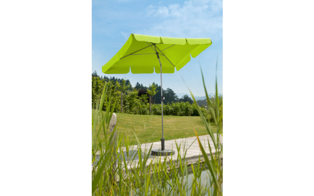 Limettengrüner Sonnenschirm geöffnet auf einem Holzdeck, Rasen und Büsche im Hintergrund, Schilf im Vordergrund und blauer Himmel mit Wolken