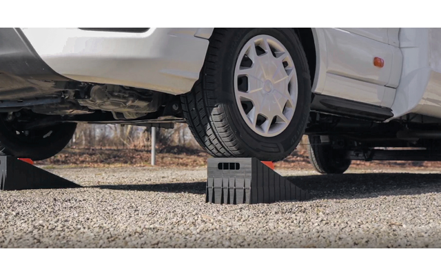 Voiture blanche, roue avant sur une rampe noire en plastique ; dessous et sol gravillonné visibles