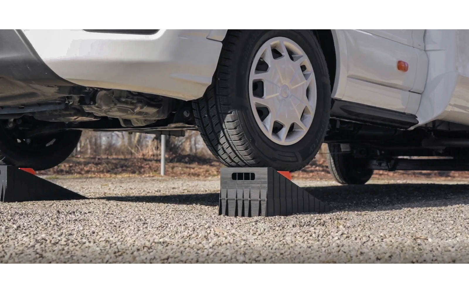 Voiture blanche, roue avant sur une rampe noire en plastique ; dessous et sol gravillonné visibles