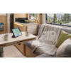 Interieur van een camper: eettafel met tablet met kaartweergave, twee mokken; kitchenette; zitplaats met deken met camperpictogram en twee kussens; raam met uitzicht op bos en bergen