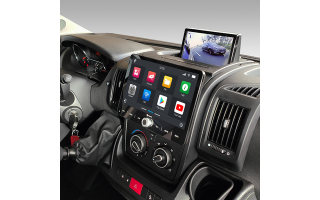 Fahrzeug-Innenraum mit Mittelkonsole, großem Touchscreen mit App-Symbolen, aufgeklapptem Monitor mit Kamerabild eines Autos und einer Straße, Schalthebel, Schlüssel im Zündschloss und Luftdüsen