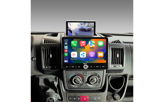 Mittelkonsole eines Fahrzeugs mit zwei Bildschirmen. Unterer Touchscreen zeigt bunte App-Symbole für Telefon, Musik, Karten, Nachrichten, Wiedergabe, Podcasts und Hörbücher. Oberer Bildschirm zeigt Rückfahrkamera mit Straße und einem Auto. Lüftungsdü