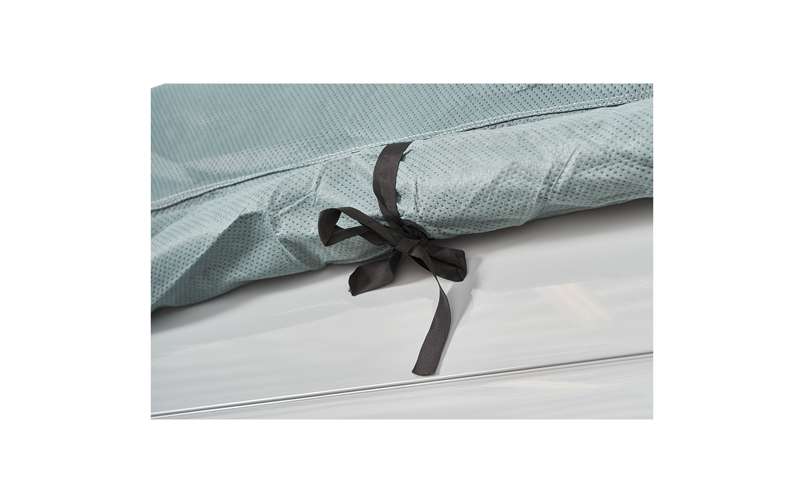 Close-up of a light green fabric with a fine dotted pattern and a black fabric bow on a white surface