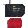 Schwarzer Stoffbeutel mit weißem Schriftzug "THERM-A-REST" und kleinem gelbem Etikett, darunter eine aufgerollte rote Matte mit schwarzem "THERM-A-REST"-Schriftzug