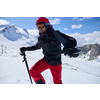 Person in roter Skihose und Helm mit Skistöcken auf schneebedecktem Berg bei Sonnenschein