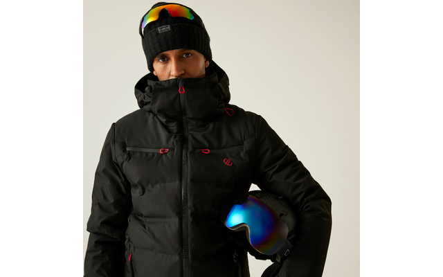 Person mit schwarzer Winterjacke, Kapuze und Skibrille auf dem Kopf, hält einen Skihelm unter dem Arm