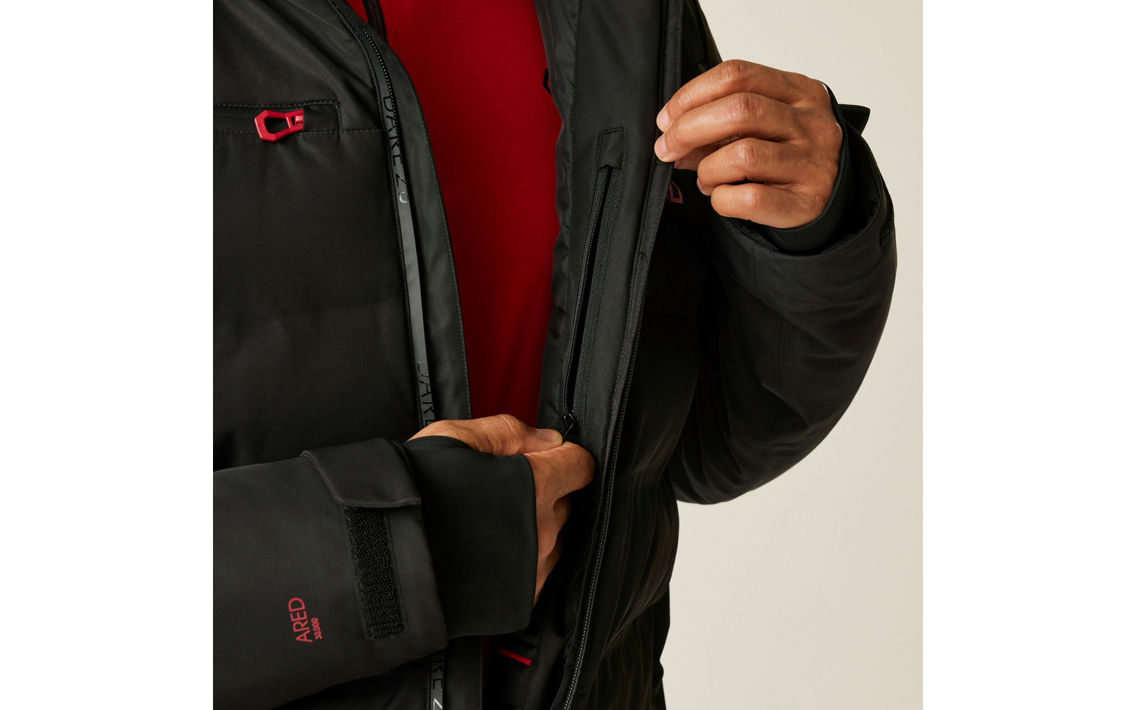 Person in schwarzer Jacke und rotem Pullover, die den Reißverschluss der Jacke hochzieht