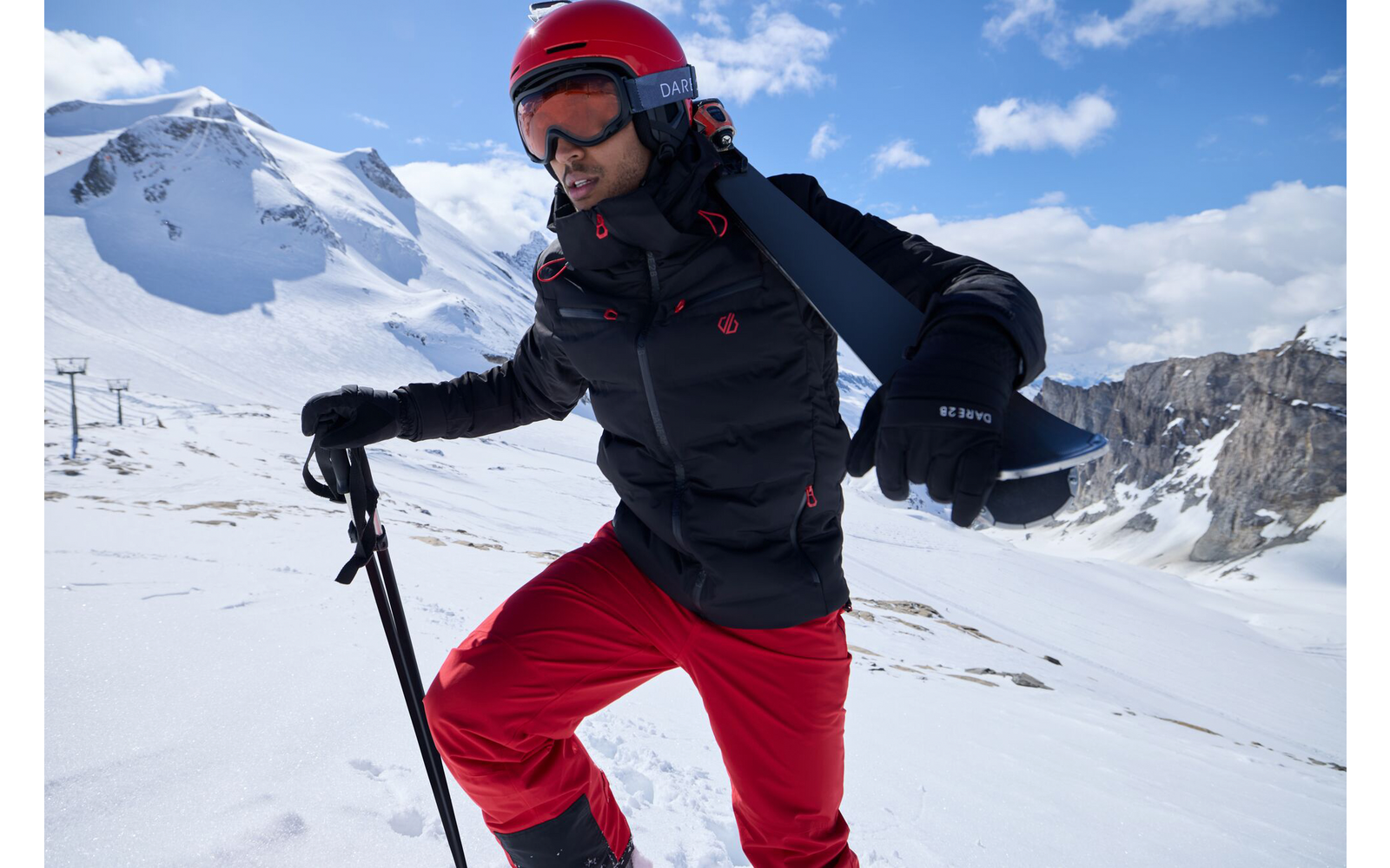 Person in roter Skihose und Helm mit Skistöcken auf schneebedecktem Berg bei Sonnenschein