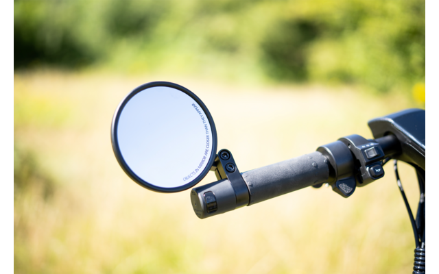 Ein Fahrradlenker mit einem runden Rückspiegel vor unscharfem, grünem Hintergrund