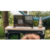 Person standing behind a table with laptop and microphone outdoors
