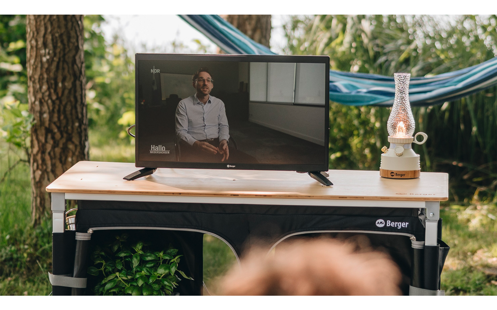 Person standing behind a table with laptop and microphone outdoors