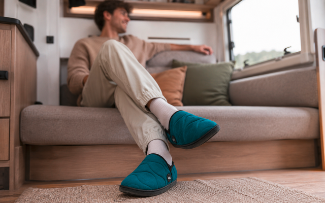 Personne assise sur la banquette d’un camping-car, jambes croisées, porte des chaussons bleu-vert