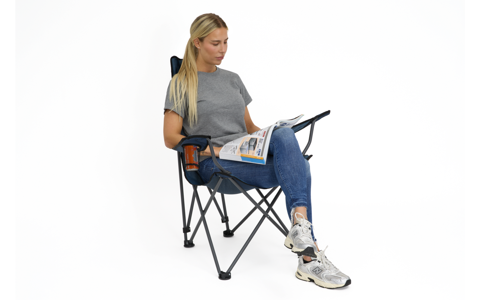 Person mit langen blonden Haaren sitzt in Klappstuhl und liest eine Zeitung