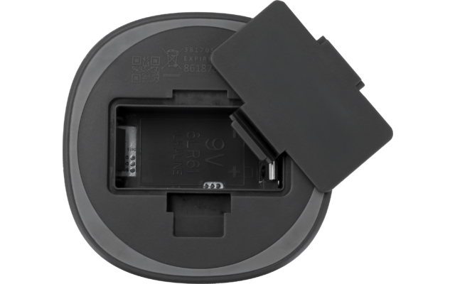 Rundes graues Gerät mit offenem rechteckigem Batteriefach, sichtbaren Metallkontakten und abgenommenem rechteckigen Deckel daneben