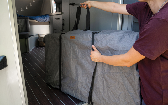 Persoon opent een grijze tas in een camper