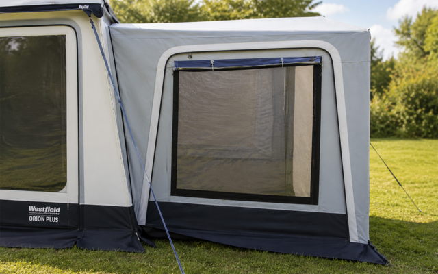 Grijze voortent met groot rechthoekig gaasraam, caravanzijwand links, gras en bomen op de achtergrond