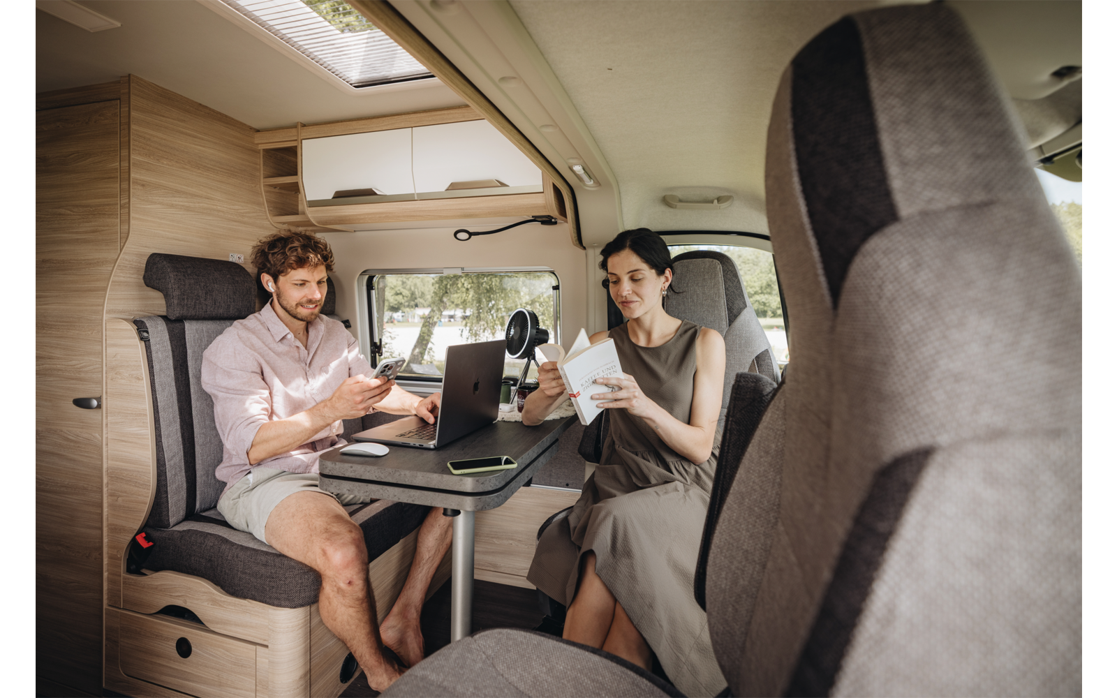 Mann und Frau sitzen an einem Tisch im Wohnmobil; Laptop auf dem Tisch; Mann hält Smartphone; Frau hält Becher